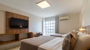 A hotel room with a large bed, a smaller bed, a TV mounted on a wooden panel, a window with curtains, and an air conditioning unit on the wall. - diRoma Exclusive Caldas Novas (Caldas Novas)