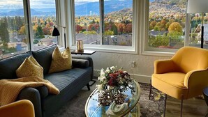 A living room with a large window offering a city view, a sofa, a yellow armchair, and a coffee table with a vase of flowers. - A Vista Villa Couples Retreat (Kelowna)