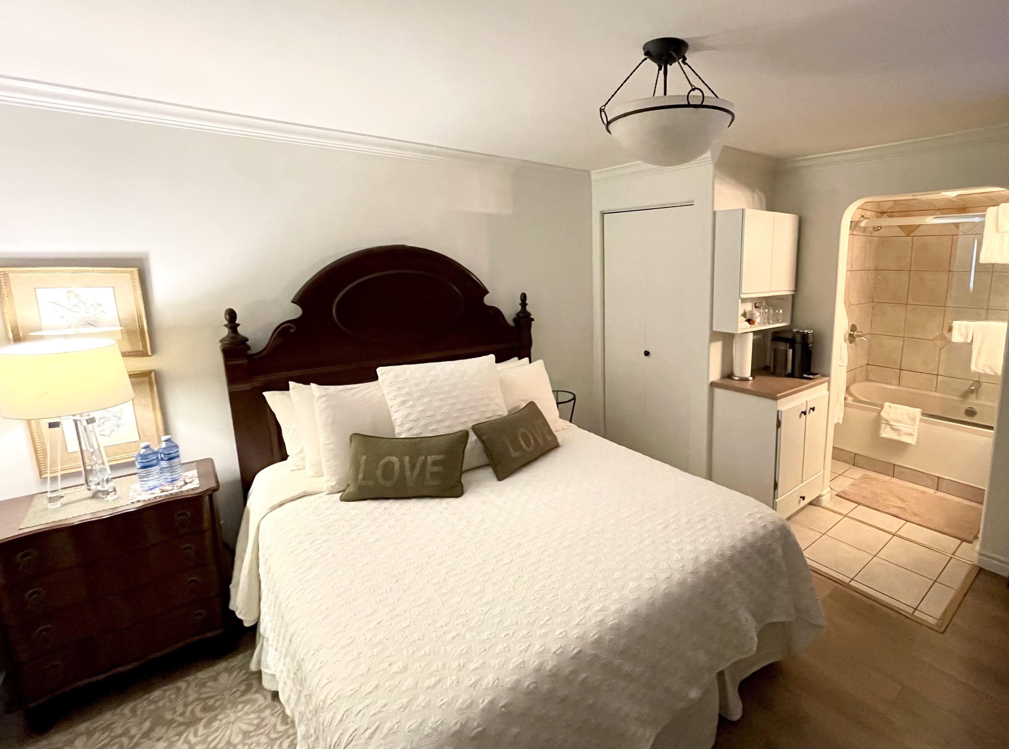 Een keurig opgemaakt slaapkamer met een bed, nachtkastje, lamp en een badkamer met bad en douche.