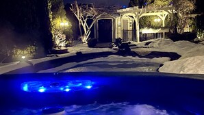 A snow-covered outdoor area with a heated pool, a wooden pergola, and a house in the background. - A Vista Villa Couples Retreat (Kelowna)