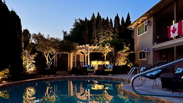 A swimming pool with a wooden deck, lounge chairs, and a covered patio area. - A Vista Villa Couples Retreat (Kelowna)