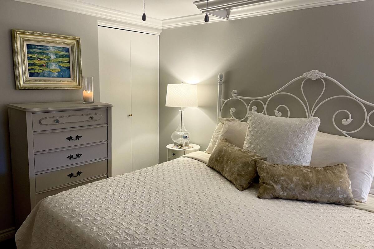 A bedroom with a bed, a dresser, a nightstand, a lamp, and a framed picture on the wall.