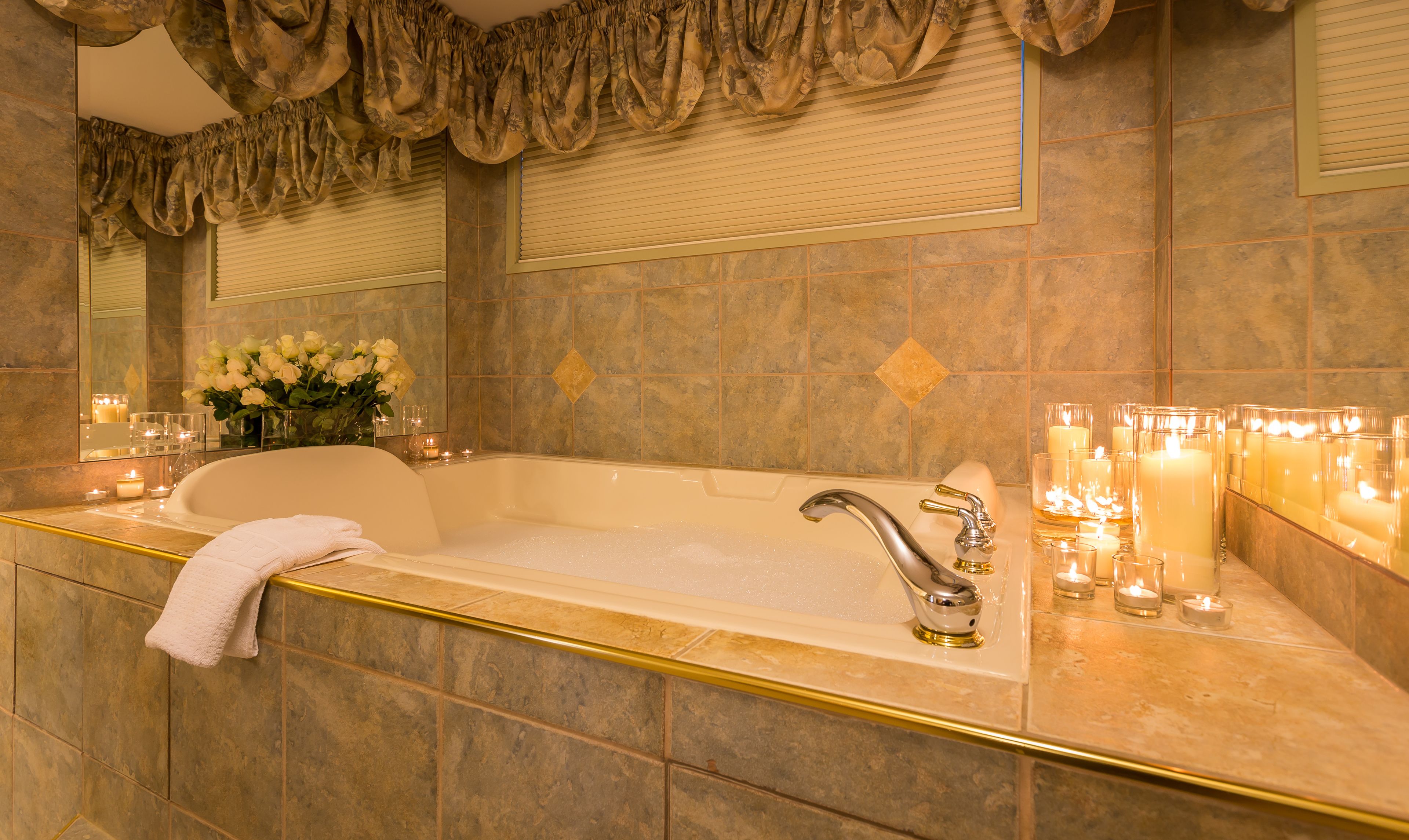 A luxurious bathroom with a large bathtub, a vanity with a mirror, and a row of candles.