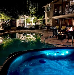 A nighttime pool area with a hot tub, lounge chairs, and a covered seating area. - A Vista Villa Couples Retreat (Kelowna)