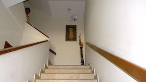 Una escalera con peldaños color beige y barandillas de madera, que conduce a un rellano con un cuadro enmarco y un florero.