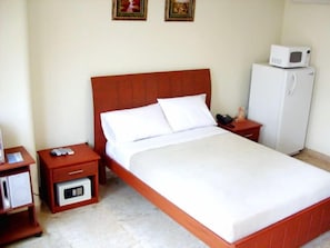 Une chambre d’hôtel avec un lit simple, une table de chevet avec un téléphone et un four à micro-ondes, ainsi qu’un petit réfrigérateur.