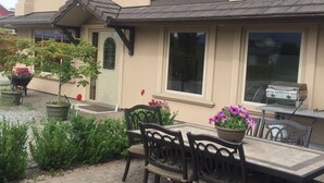 A two-story house with a patio area featuring a table and chairs, surrounded by potted plants and flowers. - All Seasons Bed & Breakfast (Kelowna)
