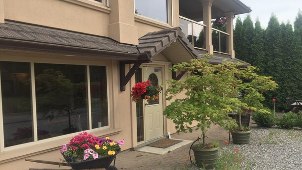 A house with a garage, a front door, and a wheelbarrow with flowers. - All Seasons Bed & Breakfast (Kelowna)