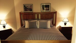 A double bed with a wooden headboard, two bedside tables with lamps, and two framed pictures on the wall. - All Seasons Bed & Breakfast (Kelowna)
