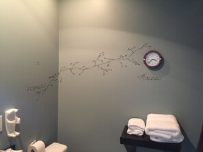 Ein Badezimmer mit einer Wanduhr, einem Handtuchhalter mit Handtüchern und einem Toilettenpapierhalter.