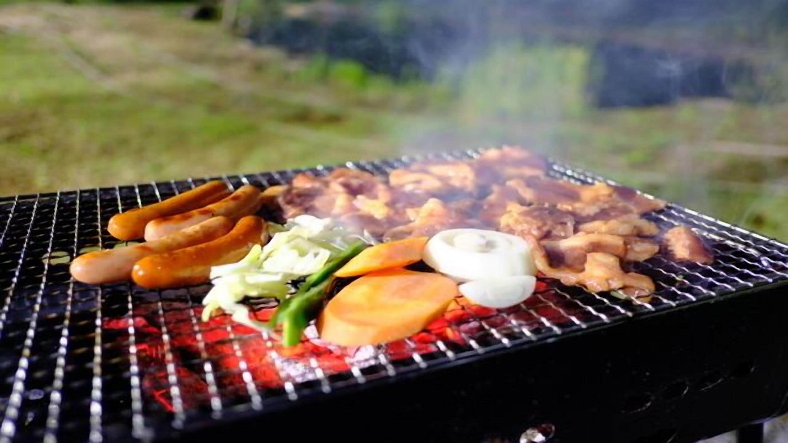 A grill with sausages, vegetables, and meat being cooked outdoors.