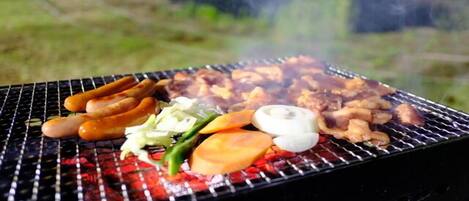 A grill with sausages, vegetables, and meat being cooked outdoors.