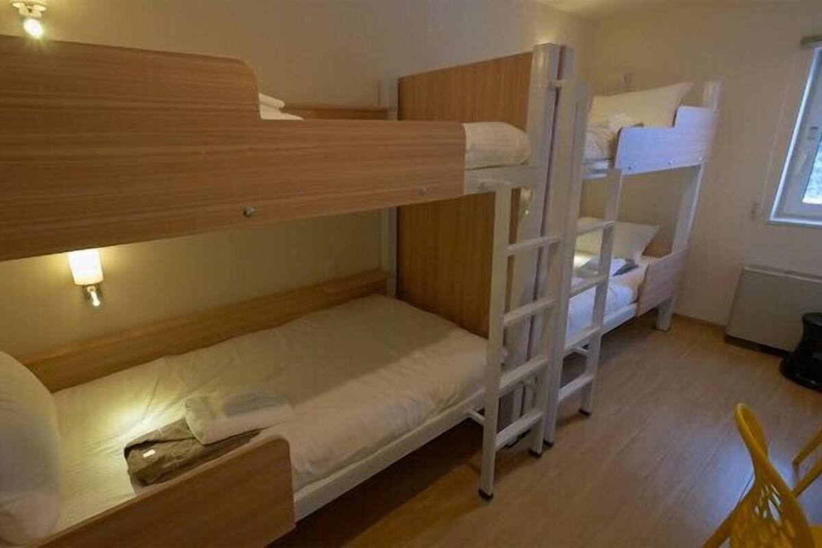 A bunk bed room with a wooden headboard, a small bedside table, and a window.