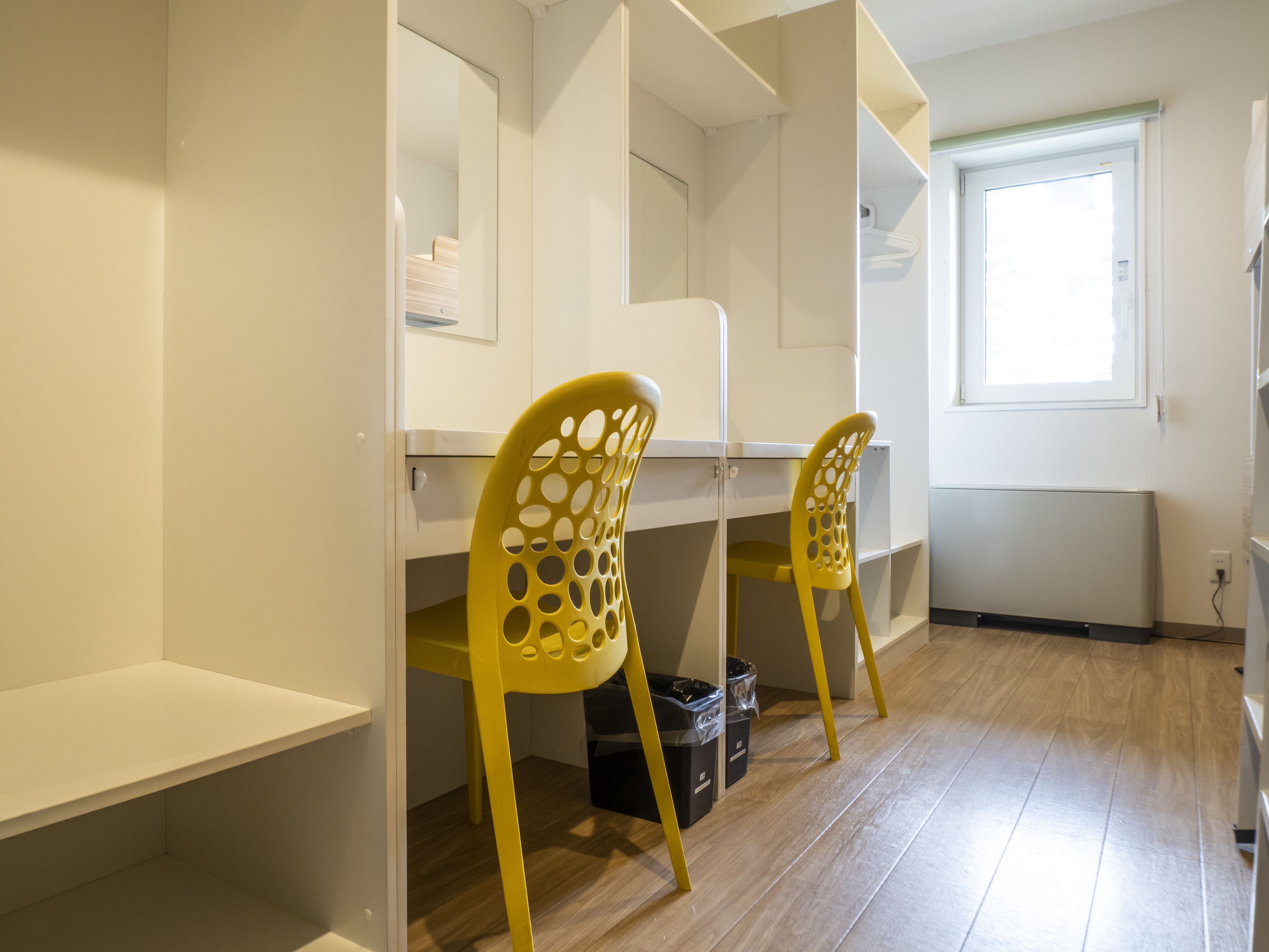 Una habitación con un escritorio, dos sillas amarillas, un radiador y una ventana.