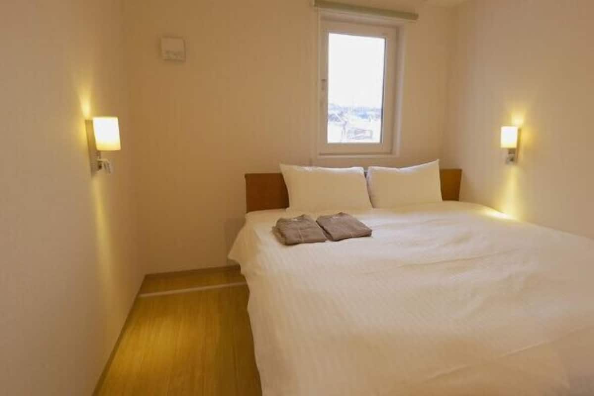 A hotel room with a bed, a window, and two wall-mounted lights.