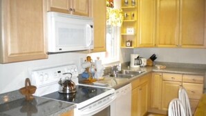 Une cuisine avec des meubles de rangement en bois, une cuisinière blanche, un four à micro-ondes et une machine à café.