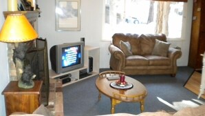 Un salon avec une télévision, un canapé, une lampe et une fenêtre avec des rideaux.