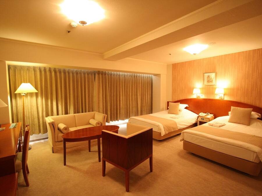 A hotel room with two beds, a sofa, a table, and a lamp.
