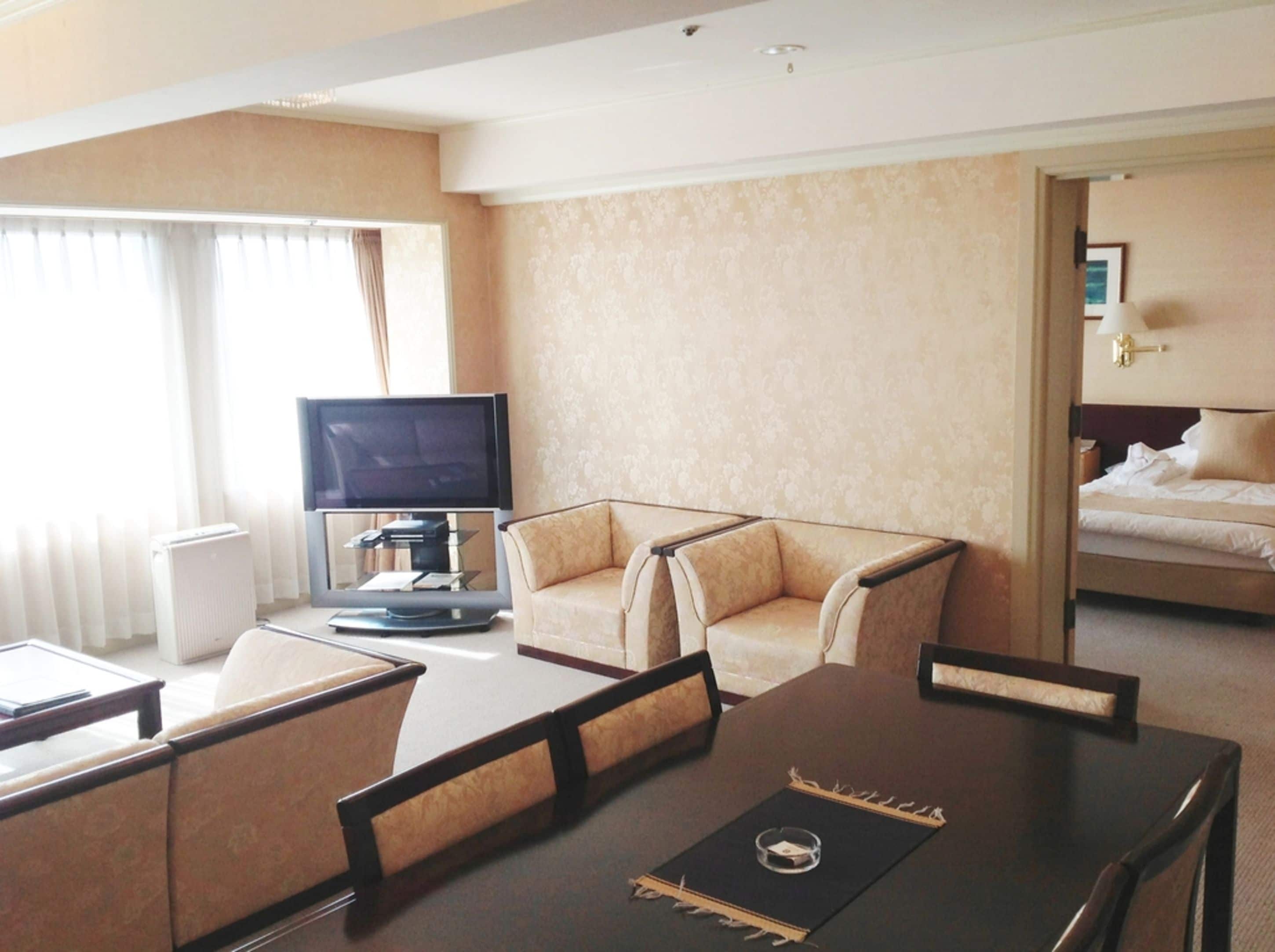 A hotel room with a bed, a TV, a sofa, and a dining table.