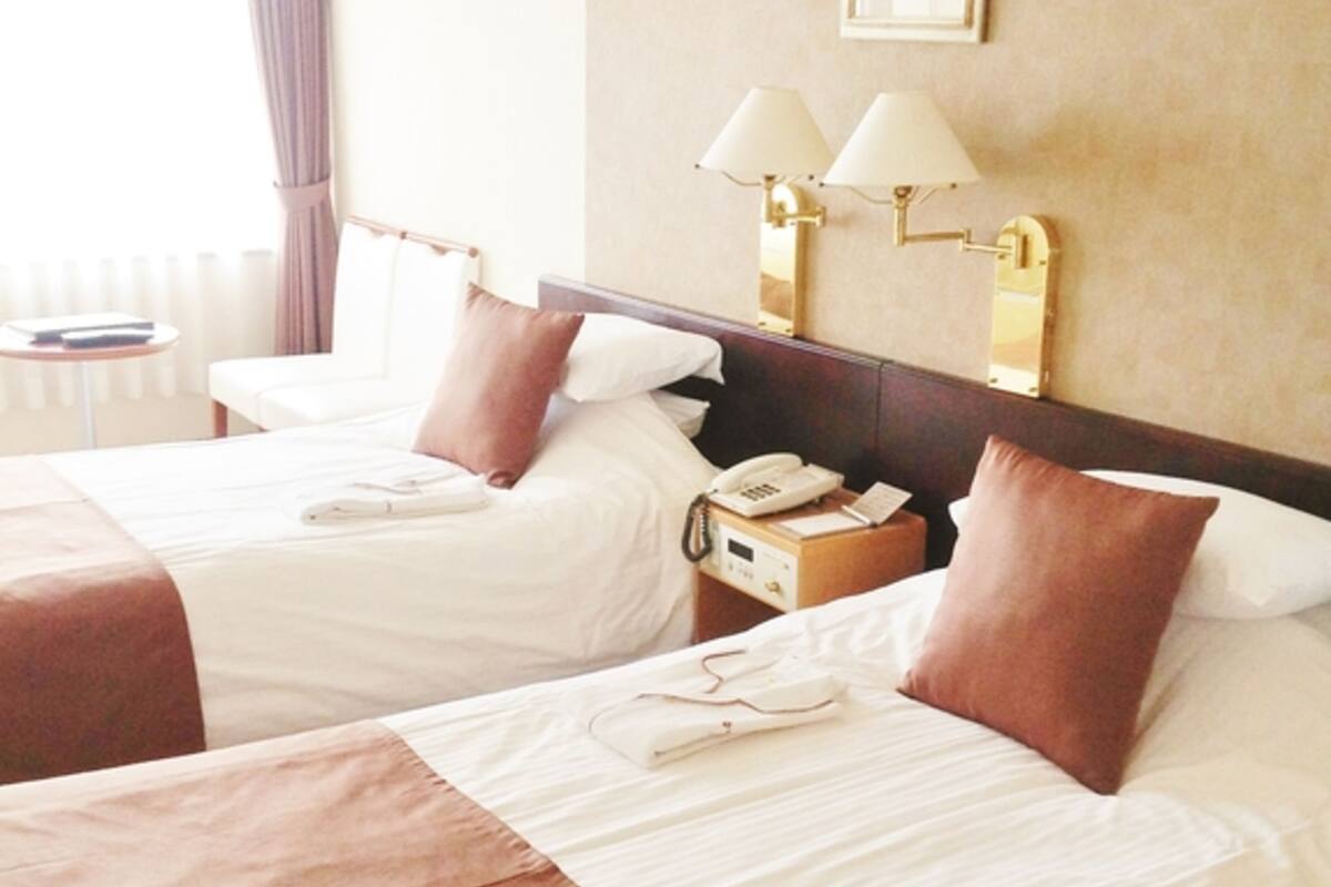 Ein Hotelzimmer mit zwei Betten, einem Nachttisch mit Lampe, einem Telefon und einem kleinen Tisch mit Stuhl.