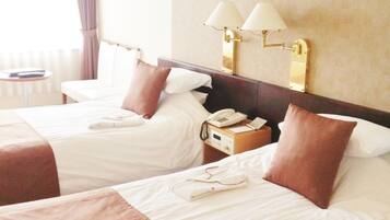 Ein Hotelzimmer mit zwei Betten, einem Nachttisch mit Lampe, einem Telefon und einem kleinen Tisch mit Stuhl.