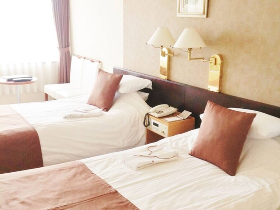 Ein Hotelzimmer mit zwei Betten, einem Nachttisch mit Lampe, einem Telefon und einem kleinen Tisch mit Stuhl.