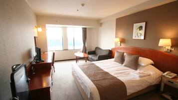 A hotel room with a bed, a desk, a chair, a TV, a lamp, and a window.