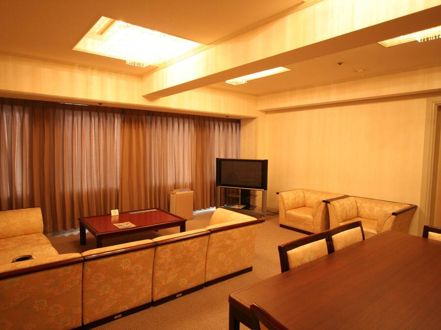 Quarto de hotel com sofá, mesa de jantar, televisão de tela plana e luminária no teto.