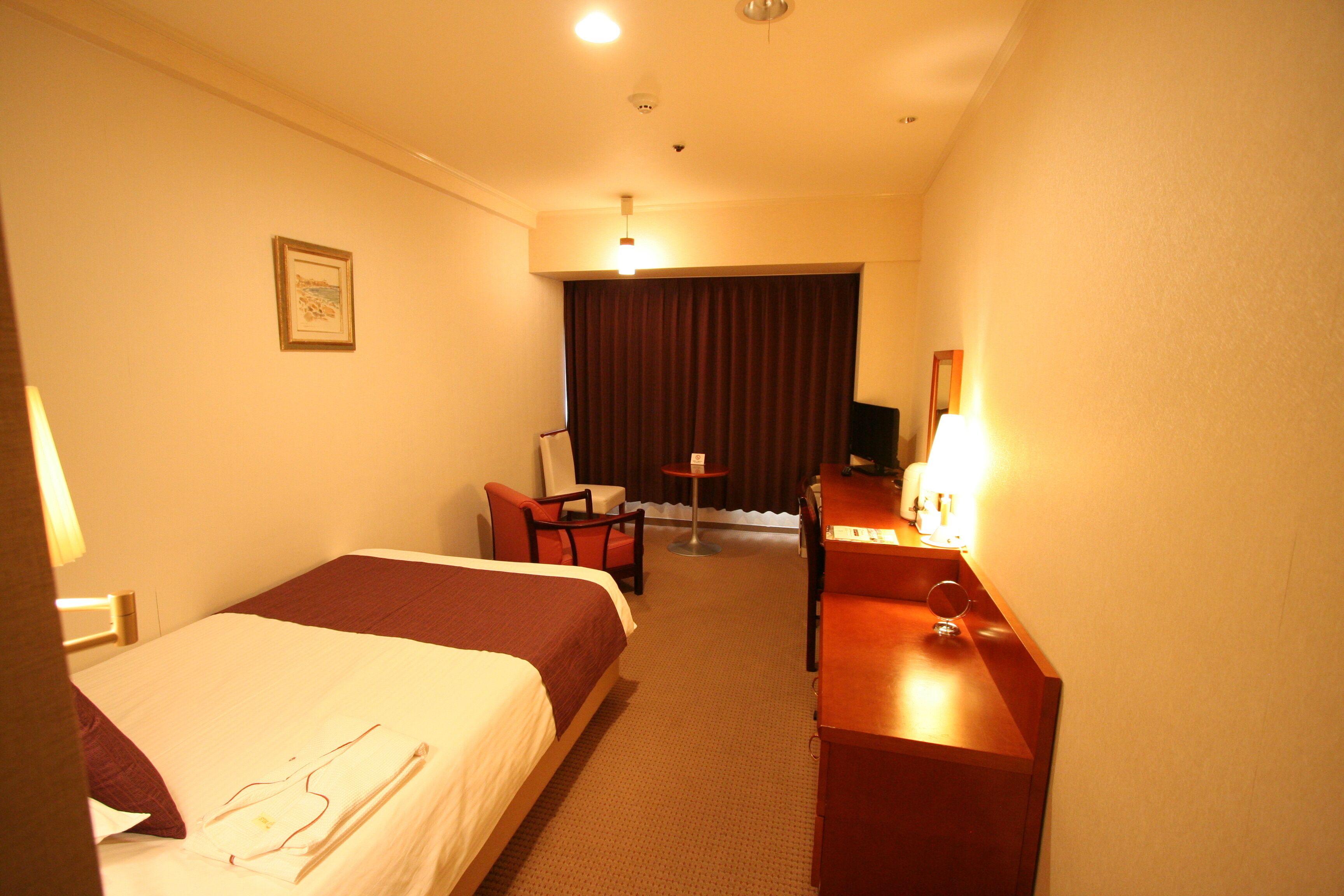 A hotel room with two beds, a desk, a chair, a small table, and a TV.