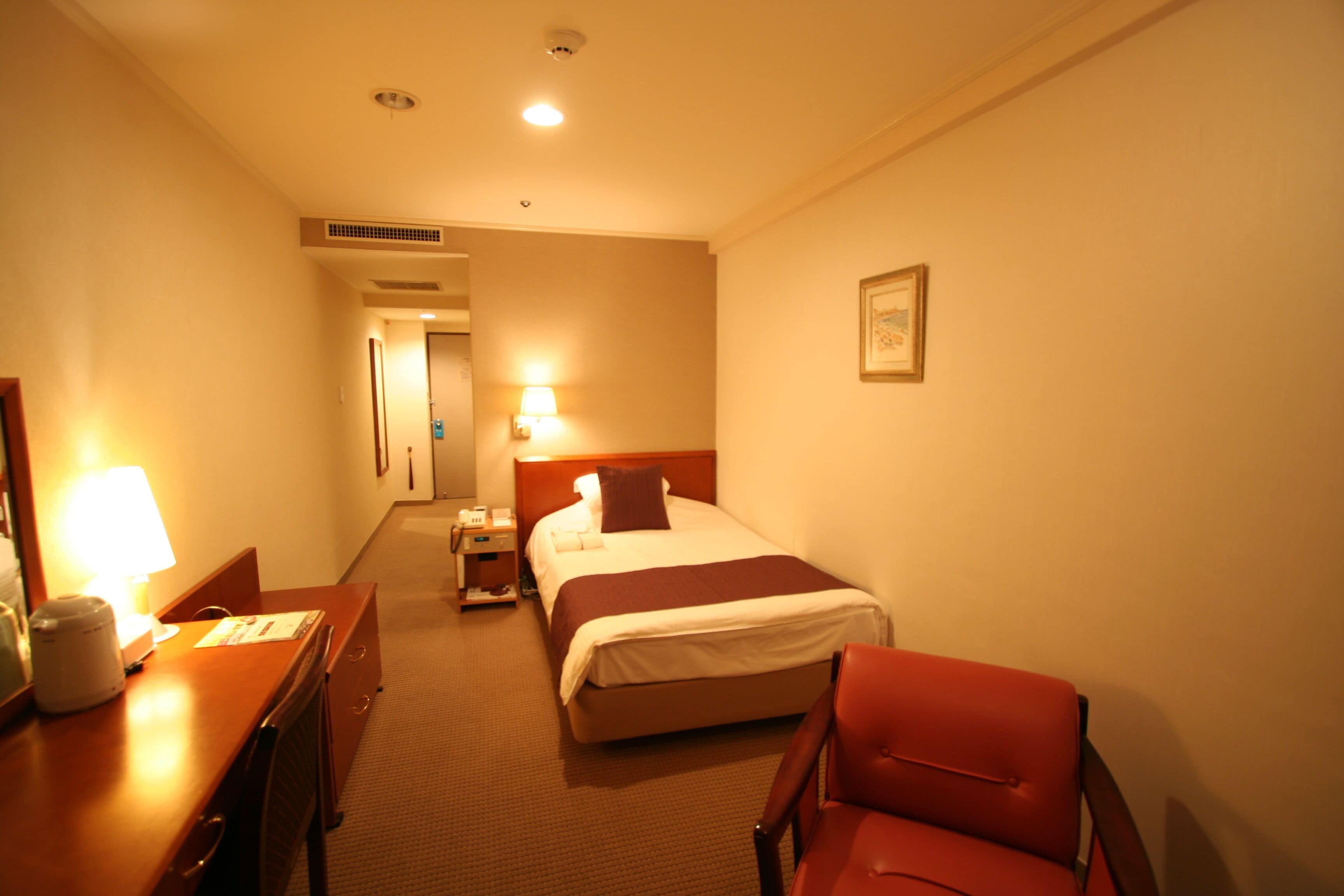 A hotel room with a bed, a desk with a lamp, a chair, and a nightstand.