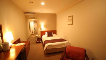 A hotel room with a bed, a desk with a lamp, a chair, and a nightstand.