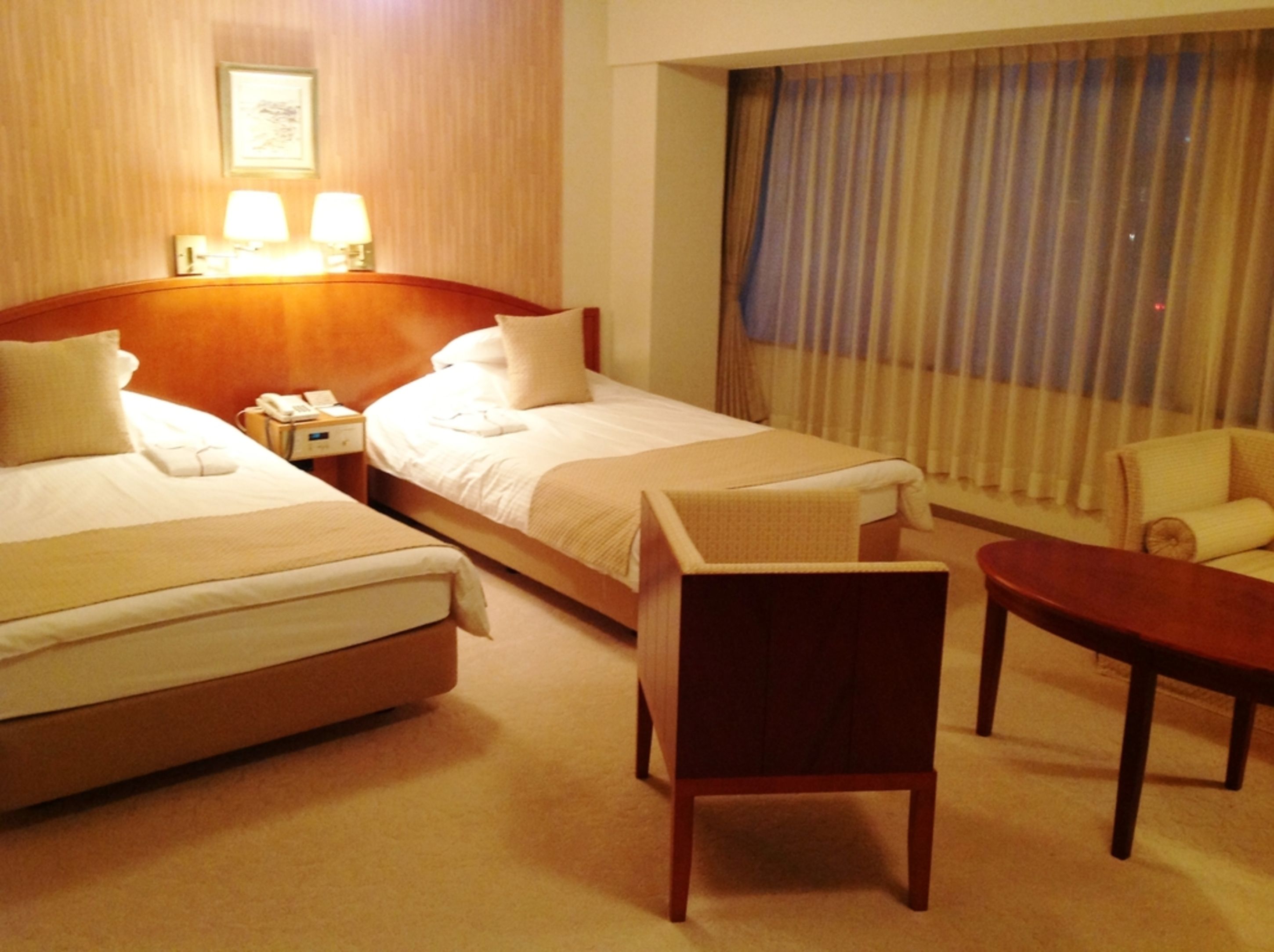 A hotel room with two beds, a desk, a chair, and a window with curtains.