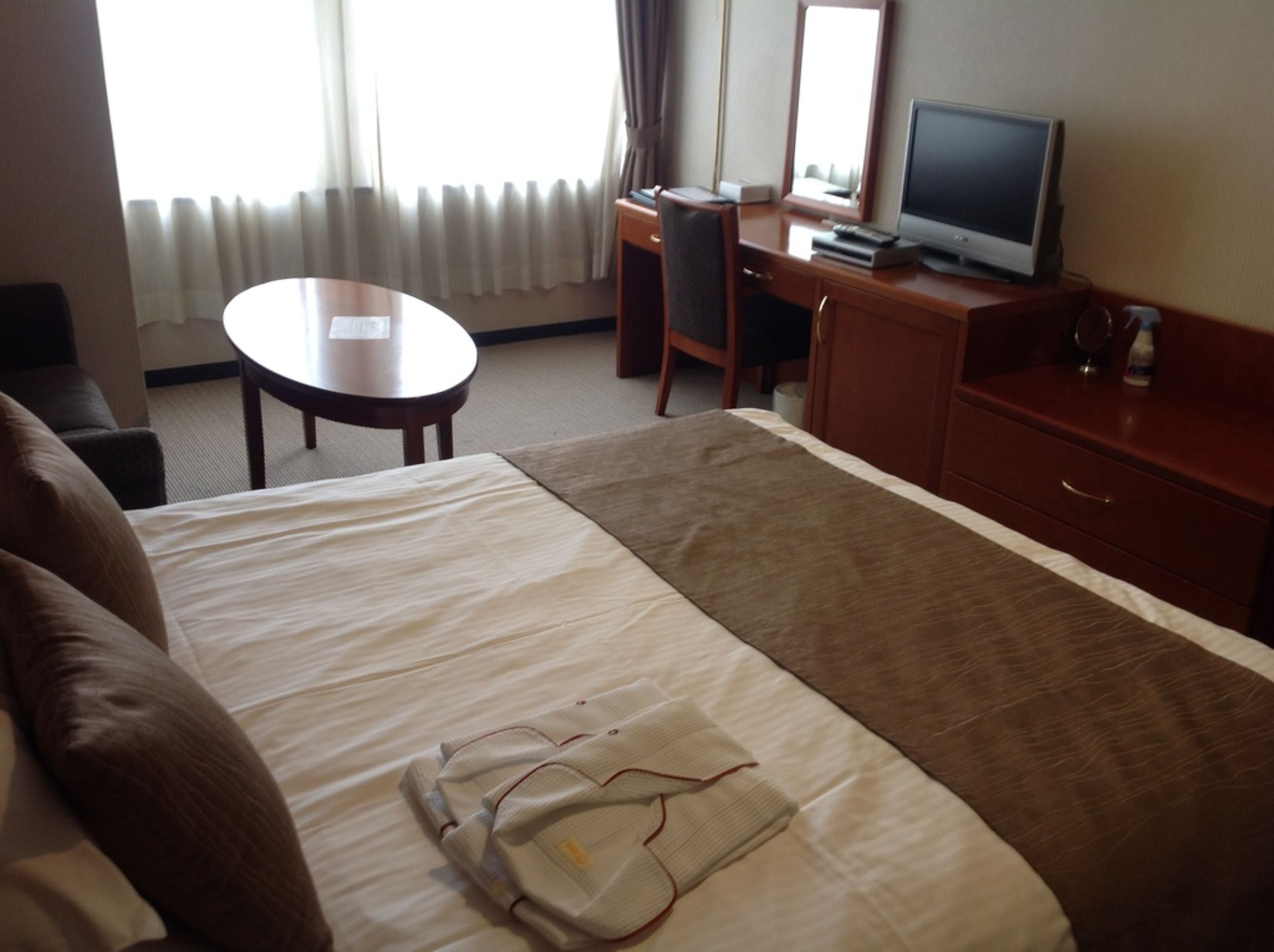 Een hotelkamer met een bed, een bureau, een stoel, een televisie en een klein tafeltje.