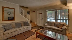 A living room with two sofas, a coffee table, a staircase, and a door leading outside. - 1200 Wildwood Unit 16 (South Lake Tahoe)