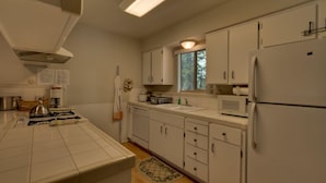 A kitchen with white cabinets, a microwave, a refrigerator, and a window. - 1200 Wildwood Unit 16 (South Lake Tahoe)