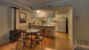 A modern kitchen with a dining area, featuring a central island, white cabinetry, and a stainless steel range hood. - 1200 Wildwood Unit 16 (South Lake Tahoe)