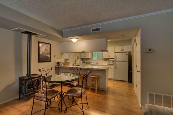 A modern kitchen with a dining area, featuring a central island, white cabinetry, and a stainless steel range hood.