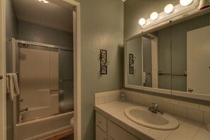 A bathroom with a shower, a sink, and a mirror with lights. - 1200 Wildwood Unit 16 (South Lake Tahoe)