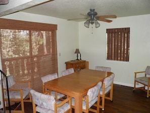 A dining area with a wooden table and six chairs, a ceiling fan, and two windows with blinds. - 1210 Timber Lane (South Lake Tahoe)