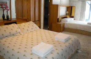 A hotel room with a large bed, a smaller bed, a desk with a lamp, and a wardrobe.