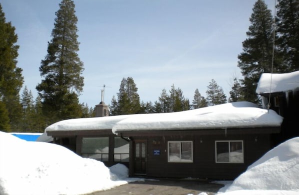 A small lodge with a snow-covered roof, surrounded by tall evergreen trees.