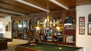 A billiards room with a pool table, multiple chandeliers, and a bookshelf filled with books and decorative items.