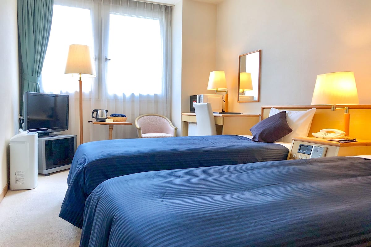 A hotel room with two beds, a desk with a computer, a television, and a telephone.