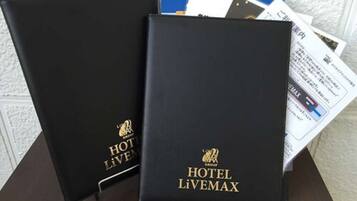 Two black leather-bound books with 'HOTEL LIVEMAX' branding, placed on a wooden surface with some papers partially visible.