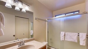 Baño con lavabo, espejo y ducha con mampara de vidrio.