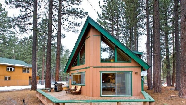 Una cabaña con techo verde y fachada de madera, rodeada de altos pinos.