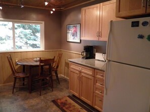 A kitchen with wooden cabinets, a refrigerator, a coffee maker, and a dining table with chairs. - 1347 Chinquapin (South Lake Tahoe)