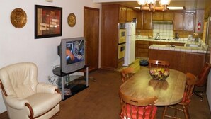 A dining area with a wooden table and chairs, a television on a stand, and a kitchen in the background. - 1421 Meadow Crest Drive (South Lake Tahoe)