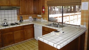 A kitchen with wooden cabinets, a dishwasher, a coffee maker, and a window with a view of the outside. - 1421 Meadow Crest Drive (South Lake Tahoe)