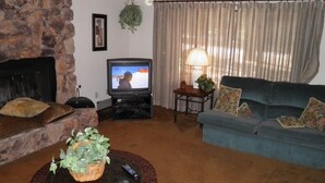 A living room with a stone fireplace, a television, a blue sofa, and a small table with a lamp. - 1421 Meadow Crest Drive (South Lake Tahoe)